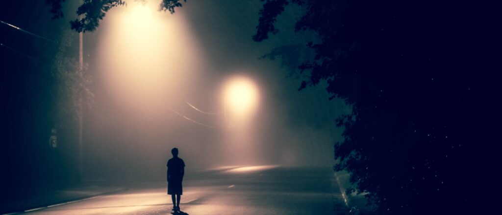 Person standing alone in the middle of a dark street.